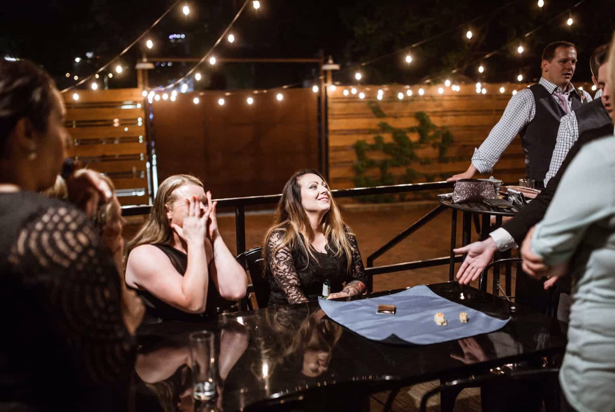 small group of spectators surprised and amazed at close up table magic at night by magician Jon Finch outside upscale restaurant