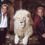Siegfried & Roy illusionists sitting on either side of white lion